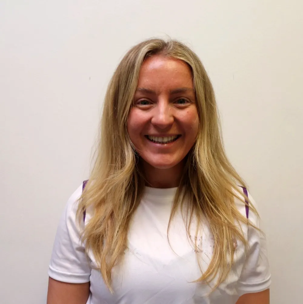 Lucy, founder and head coach of Sirens Netball Club, smiling in a white sports T-shirt
